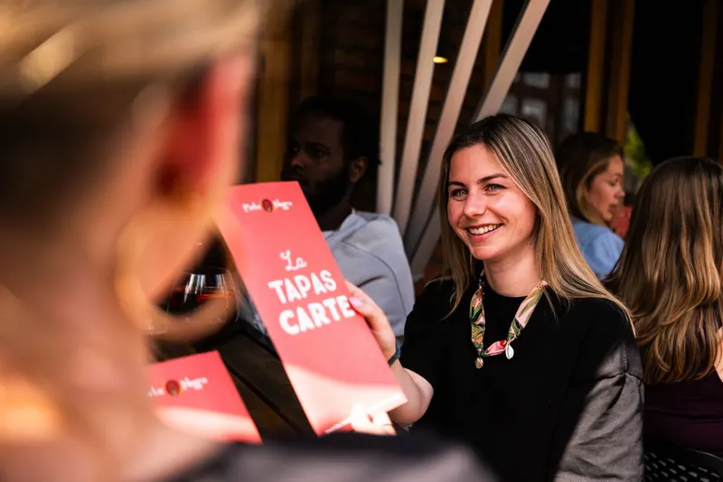 Een gast krijgt lachend de tapaskaart aangereikt