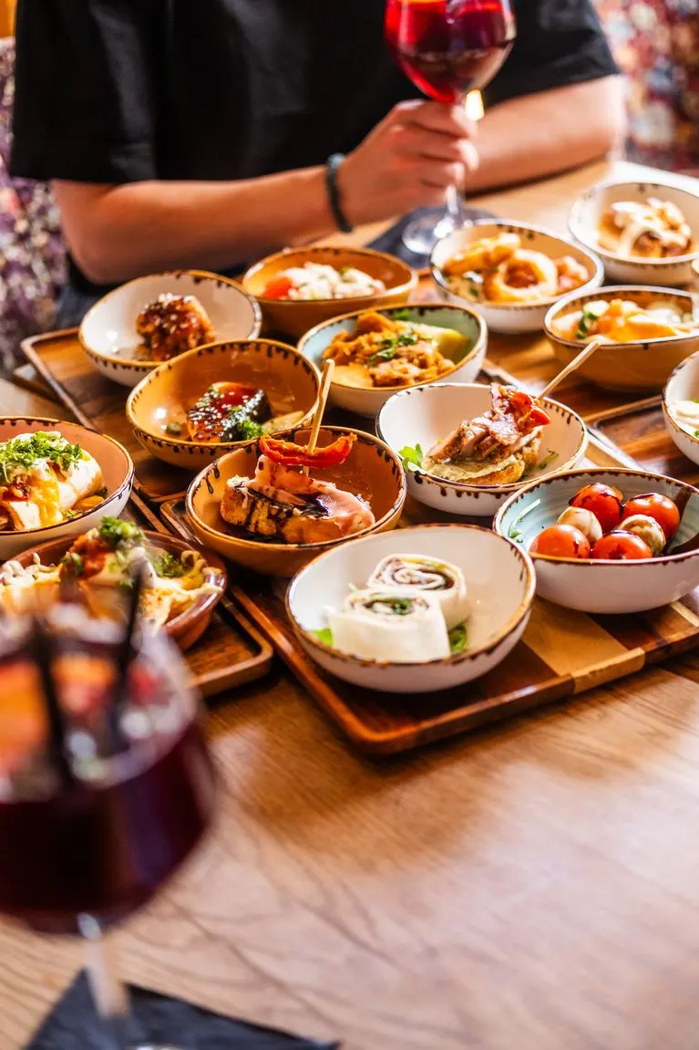Een tafel vol schaaltjes tapas op houten plankjes, met een glas rode wijn